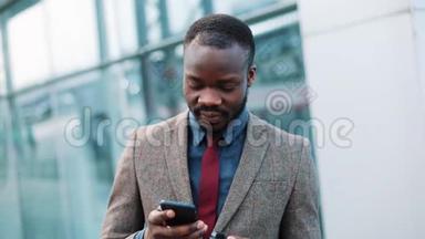疲惫的非裔美国商人站在外面的智能手机的智能手机里的东西。 使用应用程序发送短信